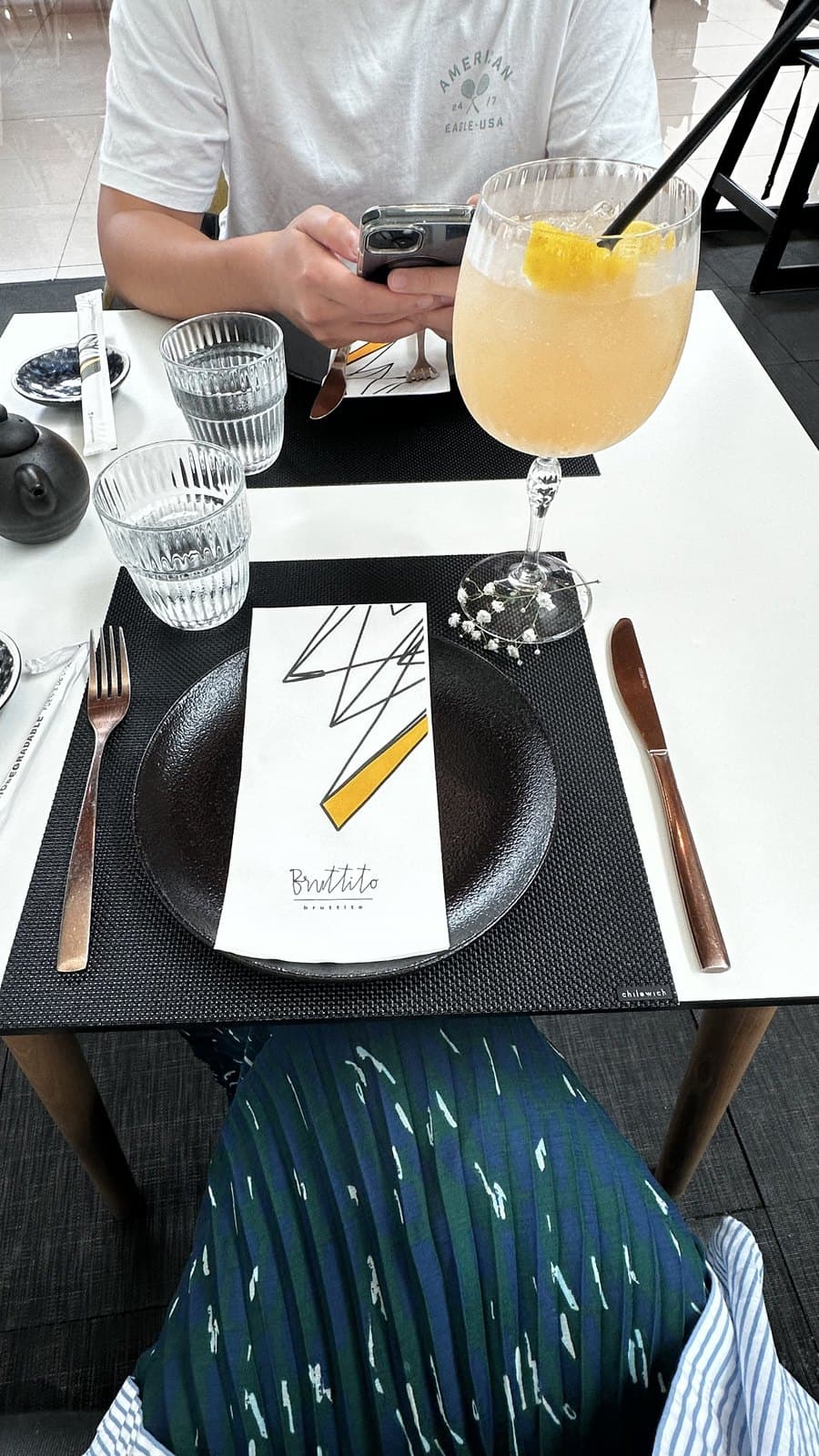 An elderflower spritz on the table at Bruttito, Multiplaza, beside a branded napkin