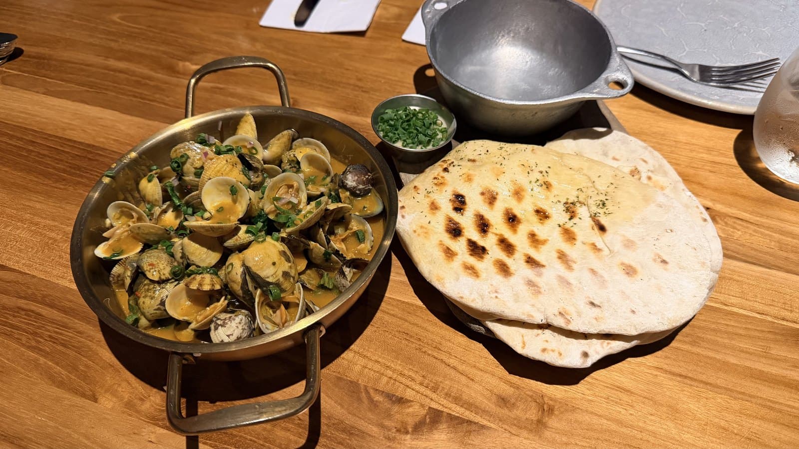 Caribbean clams at Cantina del Tigre, served over a flame in a brass pan with two grilled flatbreads and a bowl for the shells
