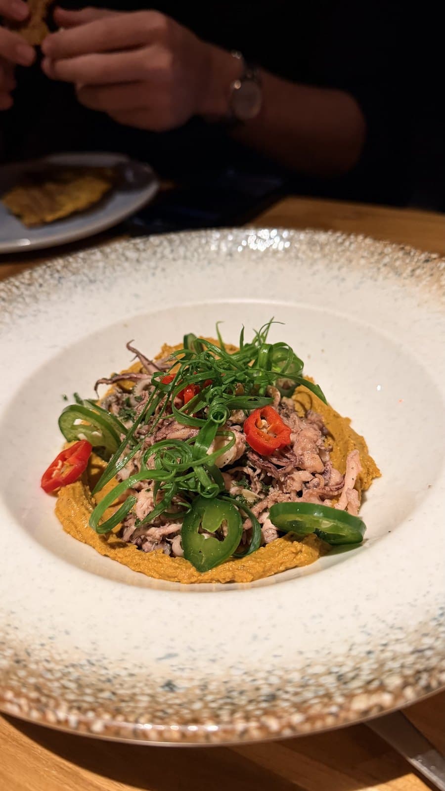 Pulled seafood over an orange purée at Cantina del Tigre, topped with jalapeño, red chilli and curled spring onion in a wide speckled bowl