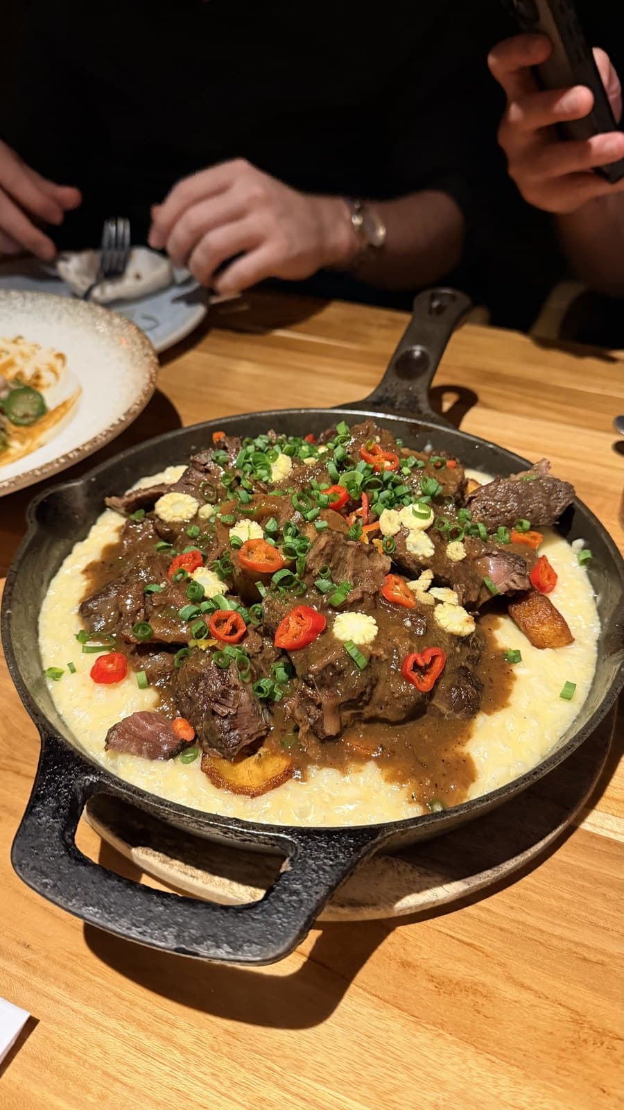 A cast-iron skillet at Cantina del Tigre: dark pieces of meat in gravy over a creamy white base, with chilli, chives and fried plantain