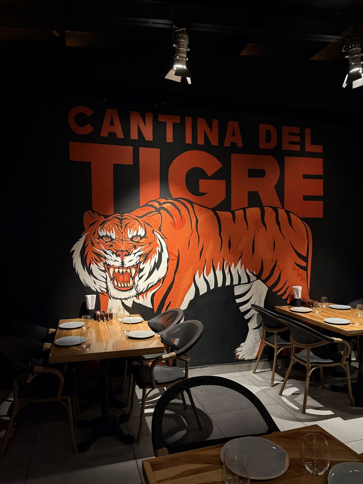 The painted orange tiger and CANTINA DEL TIGRE lettering across the black wall of the dining room, with bare wood tables laid in front of it