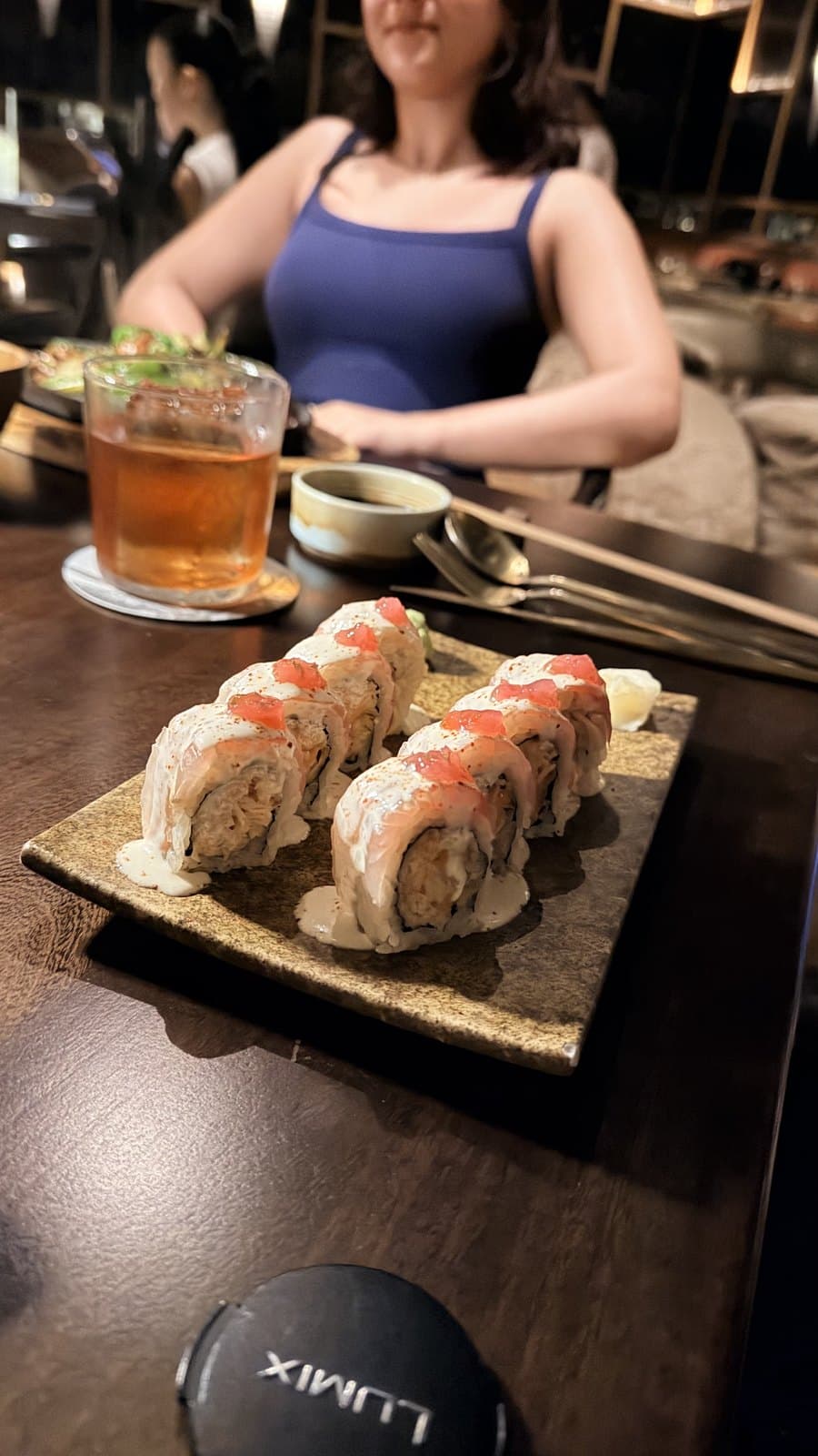 The acevichado roll at Mai Mai, topped with salmon, a pale cream and roe, on a stone plate beside a cocktail
