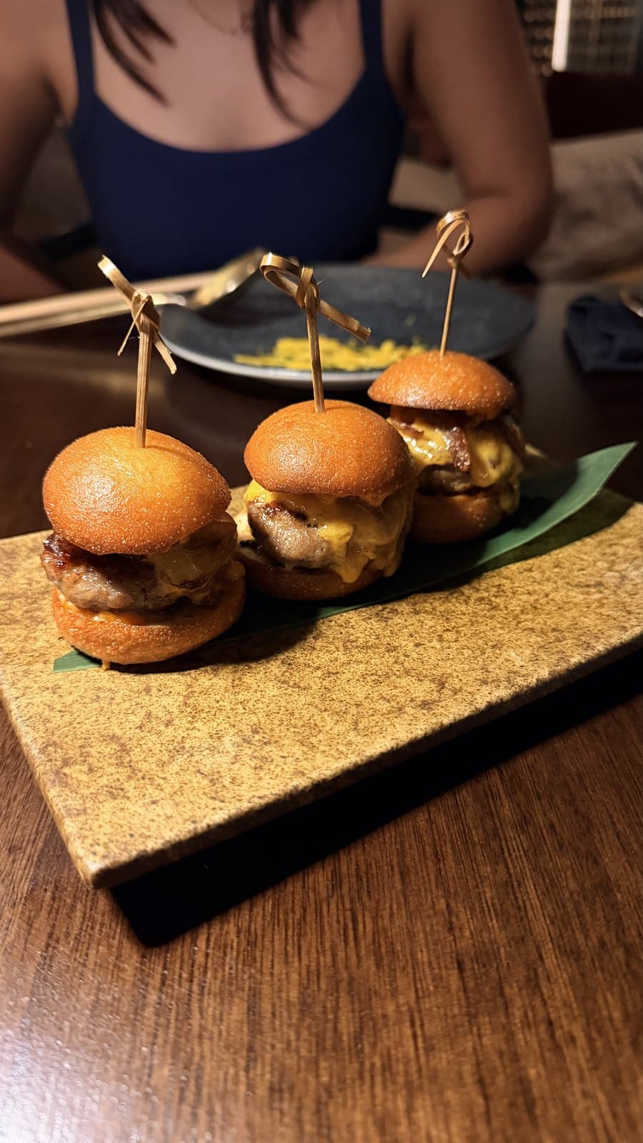 Three sliders skewered with bamboo picks on a stone board at Mai Mai