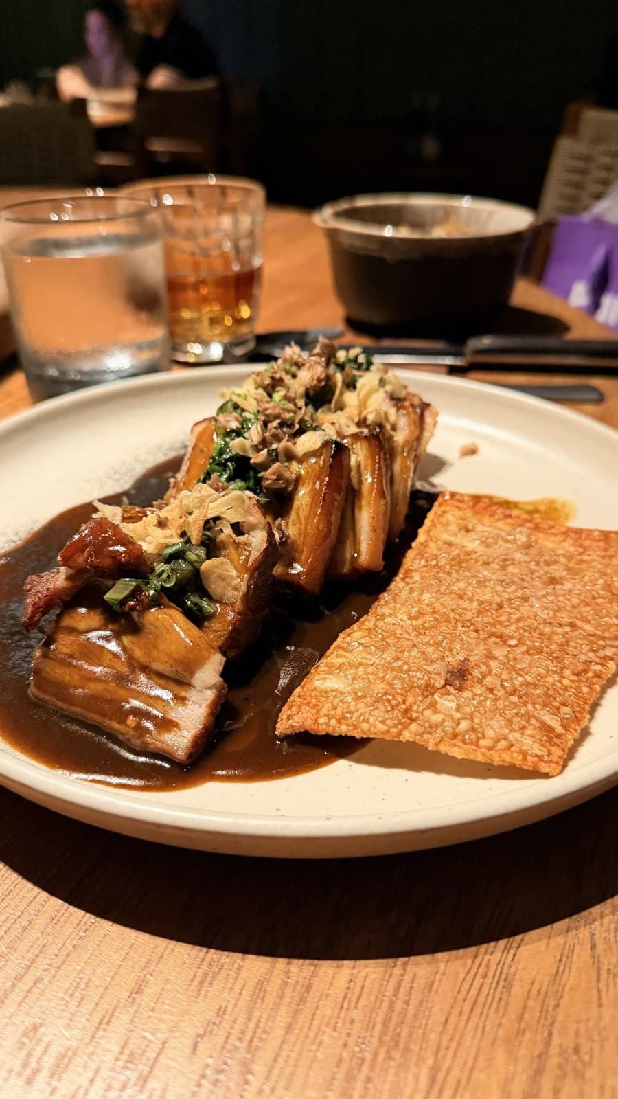 A pork main at Maito, San Francisco, Panama City: dark-glazed pieces in a pool of jus under a crisp topping and chopped greens, with a whole flat sheet of crackling beside them