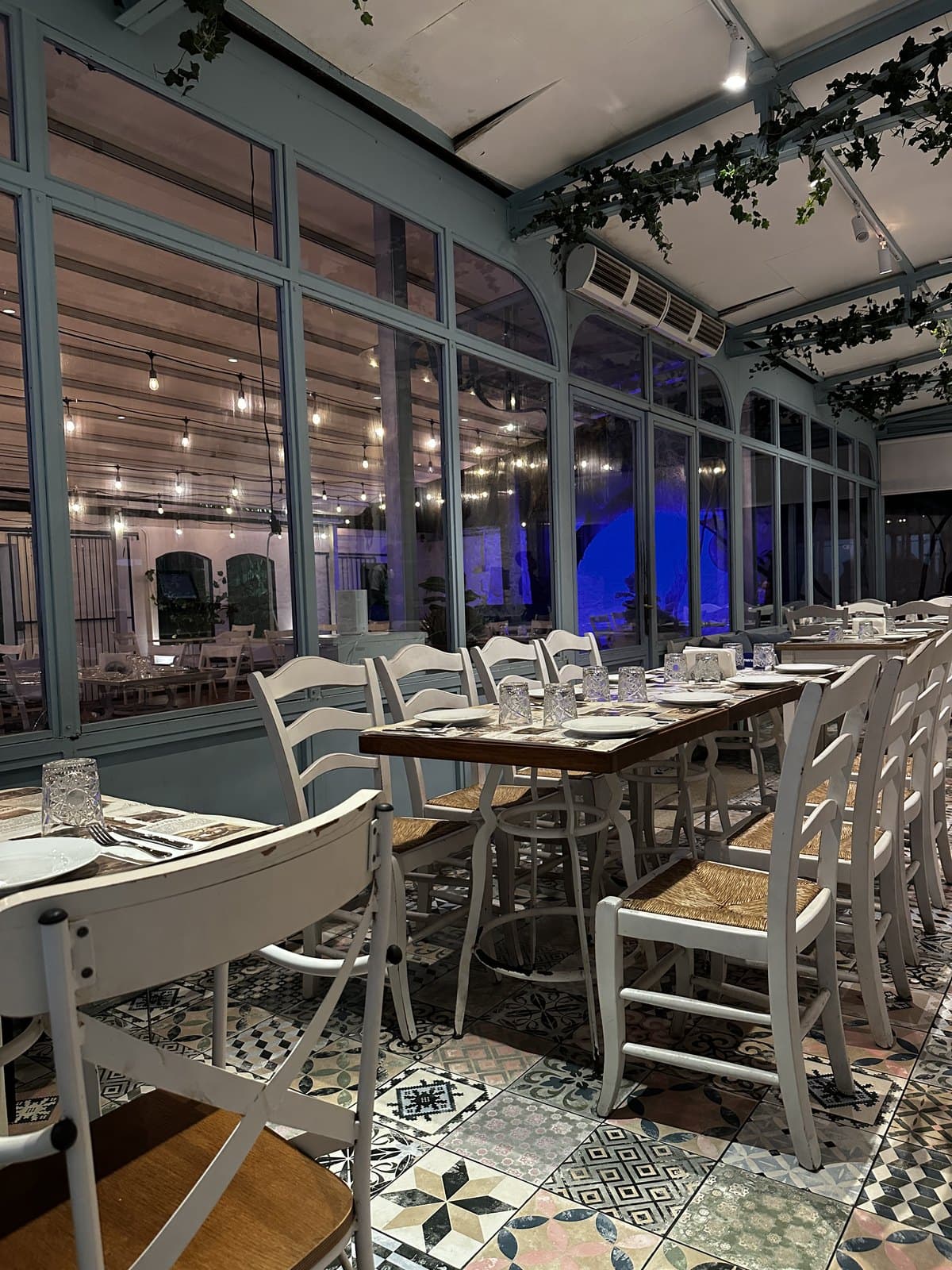 The dining room at Meze: white chairs, patterned tile floor and a wall of glass at the back