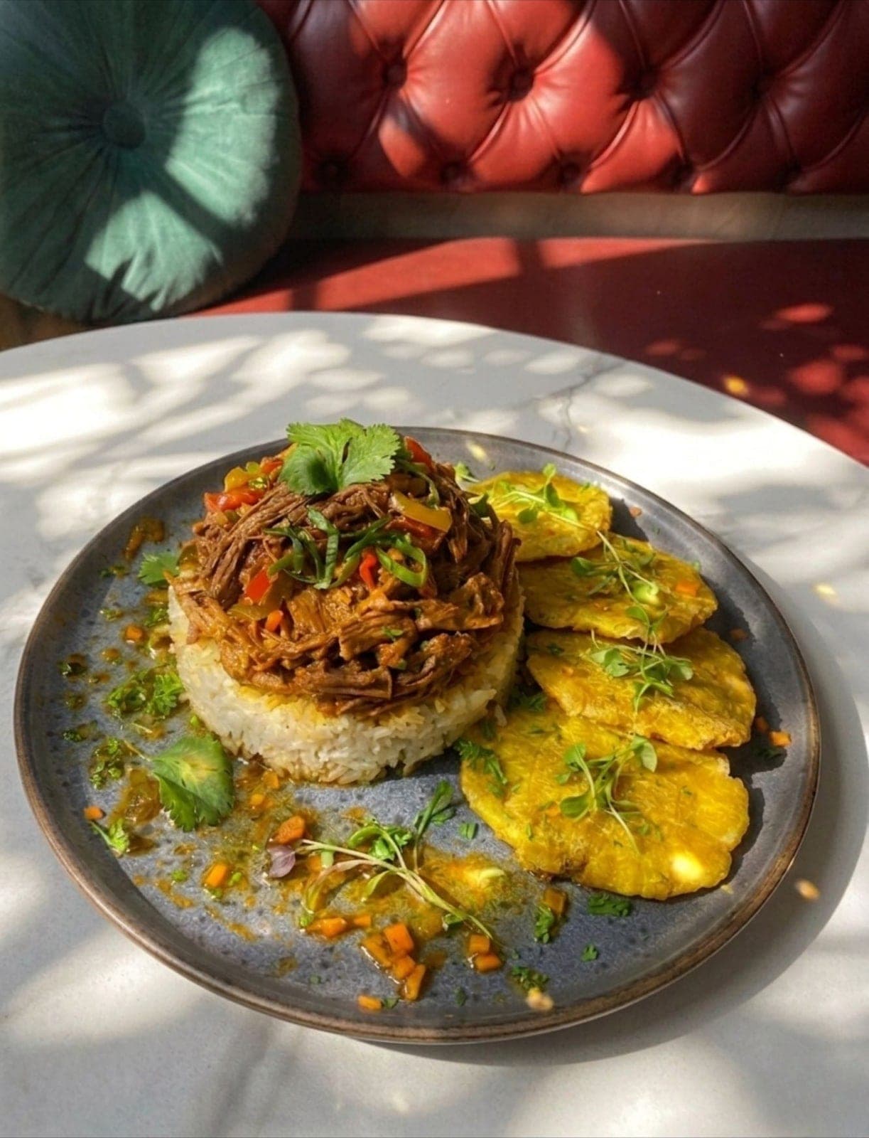Ropa vieja sobre arroz con patacones y la banca roja capitoné detrás en La Divina Comida, Casco Viejo, Ciudad de Panamá