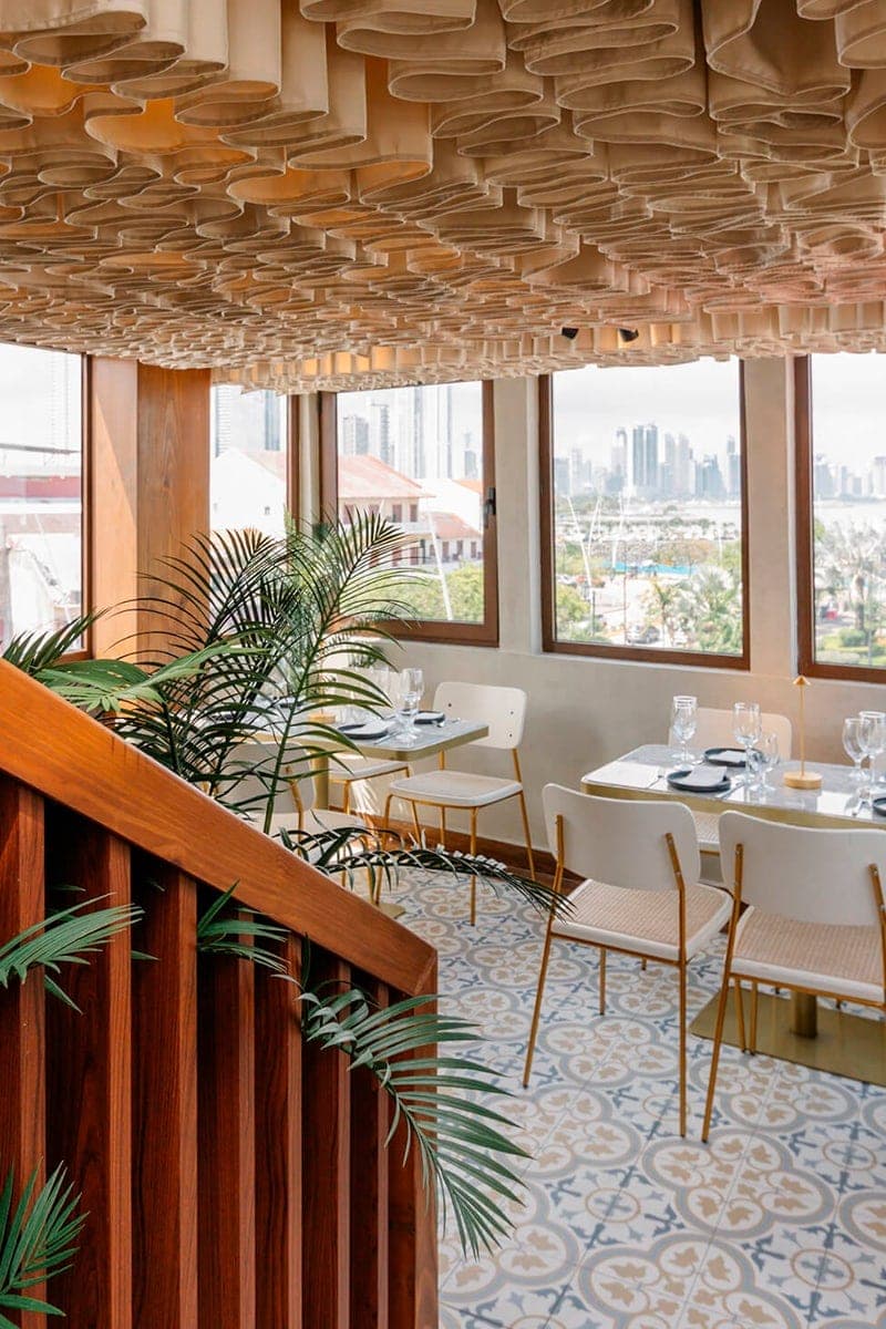 Comedor rooftop con techo de listones de madera y el horizonte de la ciudad por las ventanas en Lazotea, Casco Viejo
